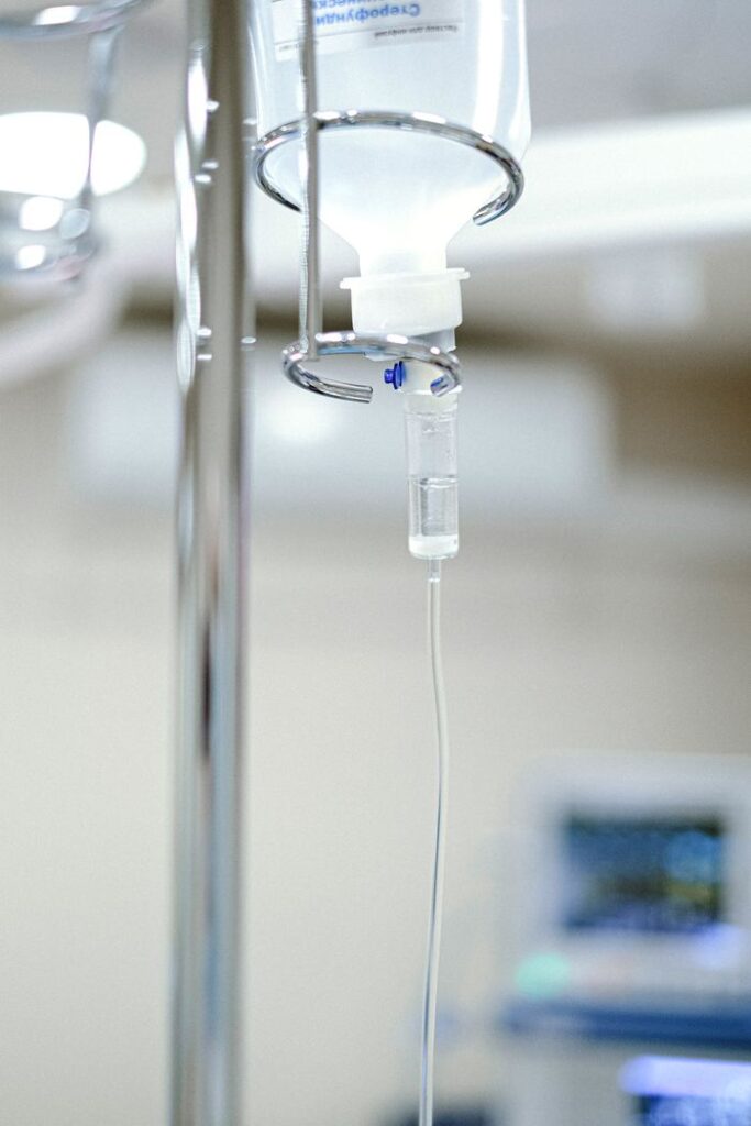 Close-up view of an IV drip chamber and stand in a clinical hospital environment.